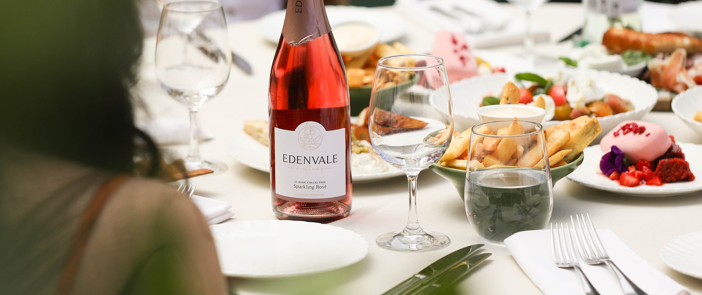 Bottle of Edenvale Rose on table full of food, glassware and cutlery 