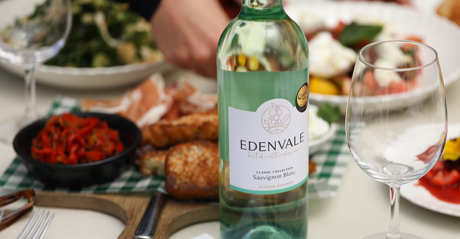 Bottle of Edenvale Sauvignon Blanc surrounded by antipasto, glasses of non-alcoholic wine,  salads and diners toasting