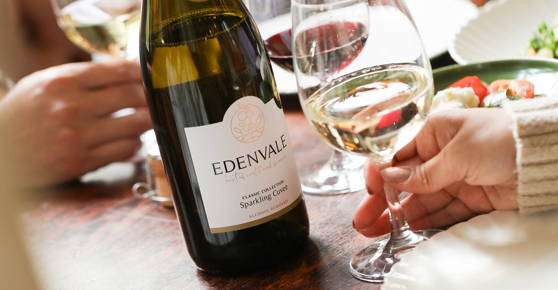 Bottle of Edenvale Sparkling Cuvee on a table with bowls of food, glasses and someone