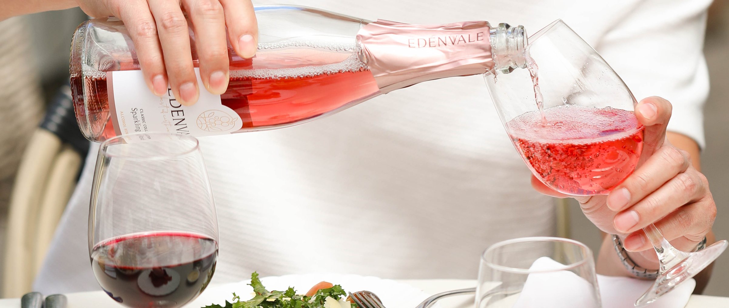 Person pouring non-alcoholic Rosé wine into a glass at an outdoor dining table